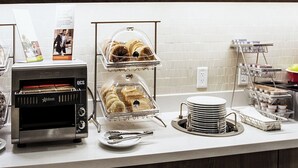 A buffet setup with a self-service oven, trays of pastries, and stacked plates. - Residence Inn Lake Charles (Lake Charles)