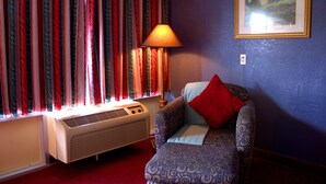A room with a patterned armchair, a red pillow, a lamp, and a window with curtains. - Lambert Inn (Kissimmee)
