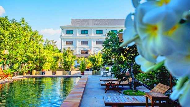 A pool area with lounge chairs and potted plants, a large building in the background, and a clear blue sky. - Galaxy Angkor Boutique Hotel (Siem Reap)