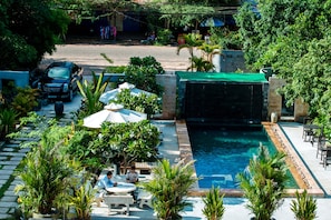 Un espace piscine agrémenté d’une cascade, entouré de verdure et doté de coins salon extérieurs.