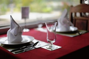 Une table dressée avec une nappe rouge, un verre transparent et des serviettes pliées.