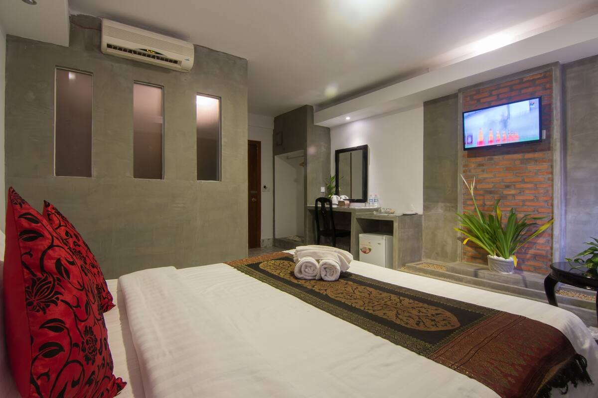 Een hotelkamer met een bed, bureau, televisie en een plant.