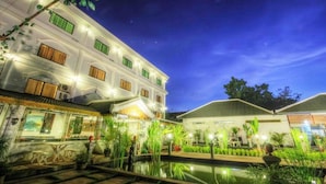 A multi-story hotel with a pool area, featuring a traditional architectural style with green window shutters and a well-lit facade. - Galaxy Angkor Boutique Hotel (Siem Reap)
