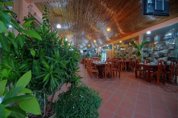 A restaurant with bamboo ceiling, green plants, and wooden tables and chairs.