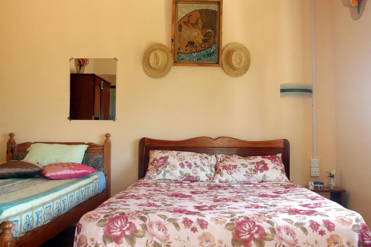 Ein Schlafzimmer mit einem hölzernen Bett, floralem Bettzeug, einem Spiegel und einem Wandbild.