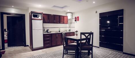 Una cocina compacta con armarios de madera oscura, un refrigerador blanco y un microondas. Hay una mesa de comedor con dos sillas y una alfombra estampada.