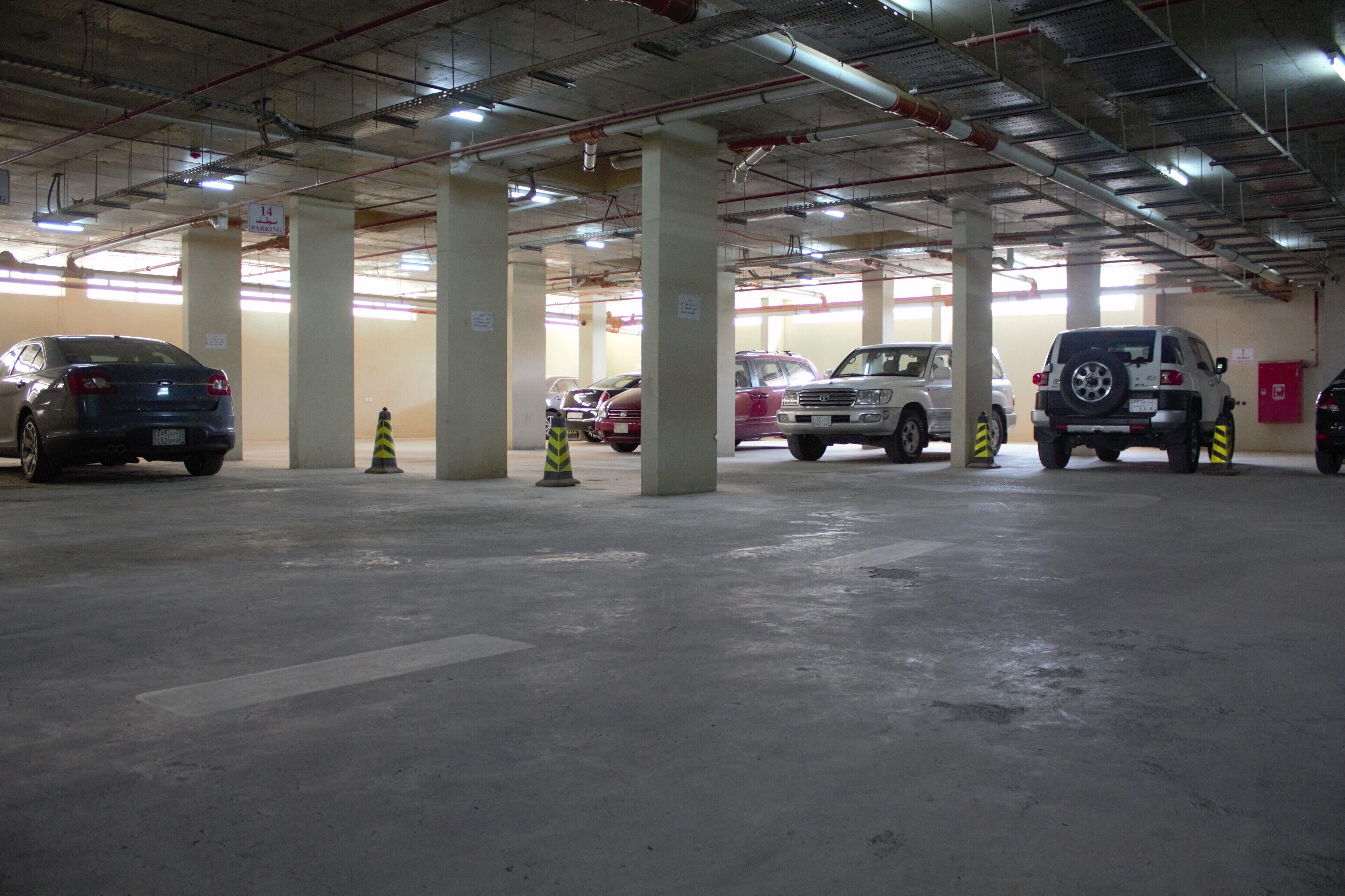 A multi-level parking garage with several cars parked, concrete pillars, and overhead lighting.