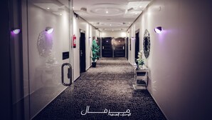 Um corredor com carpete estampado, arandelas e uma porta no final.