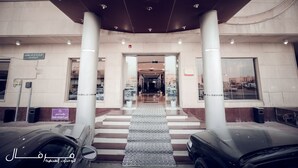 Entrada de hotel com galeria coberta, colunas imponentes e escadaria que dá acesso ao interior.