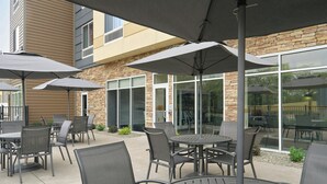 An outdoor patio area with round tables and chairs, large umbrellas, and a stone building in the background. - Fairfield Inn & Suites by Marriott Niagara Falls (Niagara Falls)