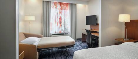 A hotel room with a bed, a desk, a chair, a TV, and a window with curtains.