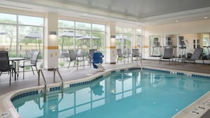 An indoor swimming pool with clear glass walls, a blue pool edge, and a seating area with tables and chairs. - Fairfield Inn & Suites by Marriott Niagara Falls (Niagara Falls)