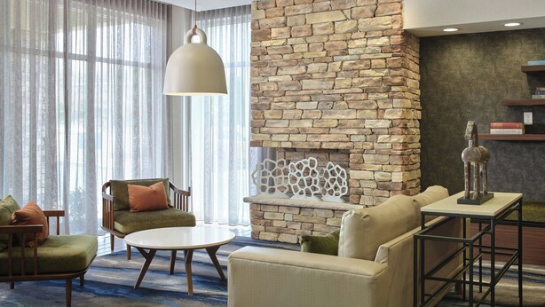 A modern living room with a stone fireplace, comfortable seating, and a large window with sheer curtains. - Fairfield Inn & Suites by Marriott Niagara Falls (Niagara Falls)