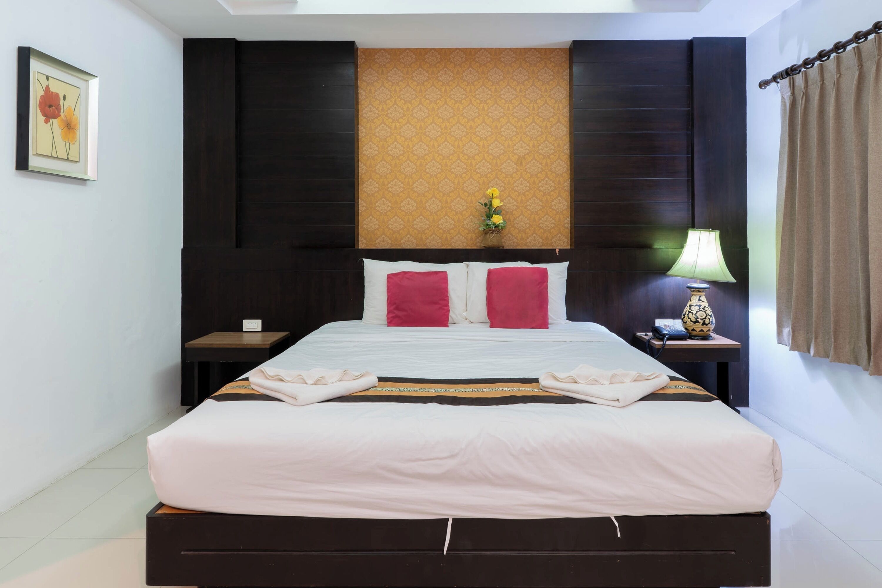 A neatly made bed with white and red bedding, a nightstand with a lamp, and a framed picture on the wall.
