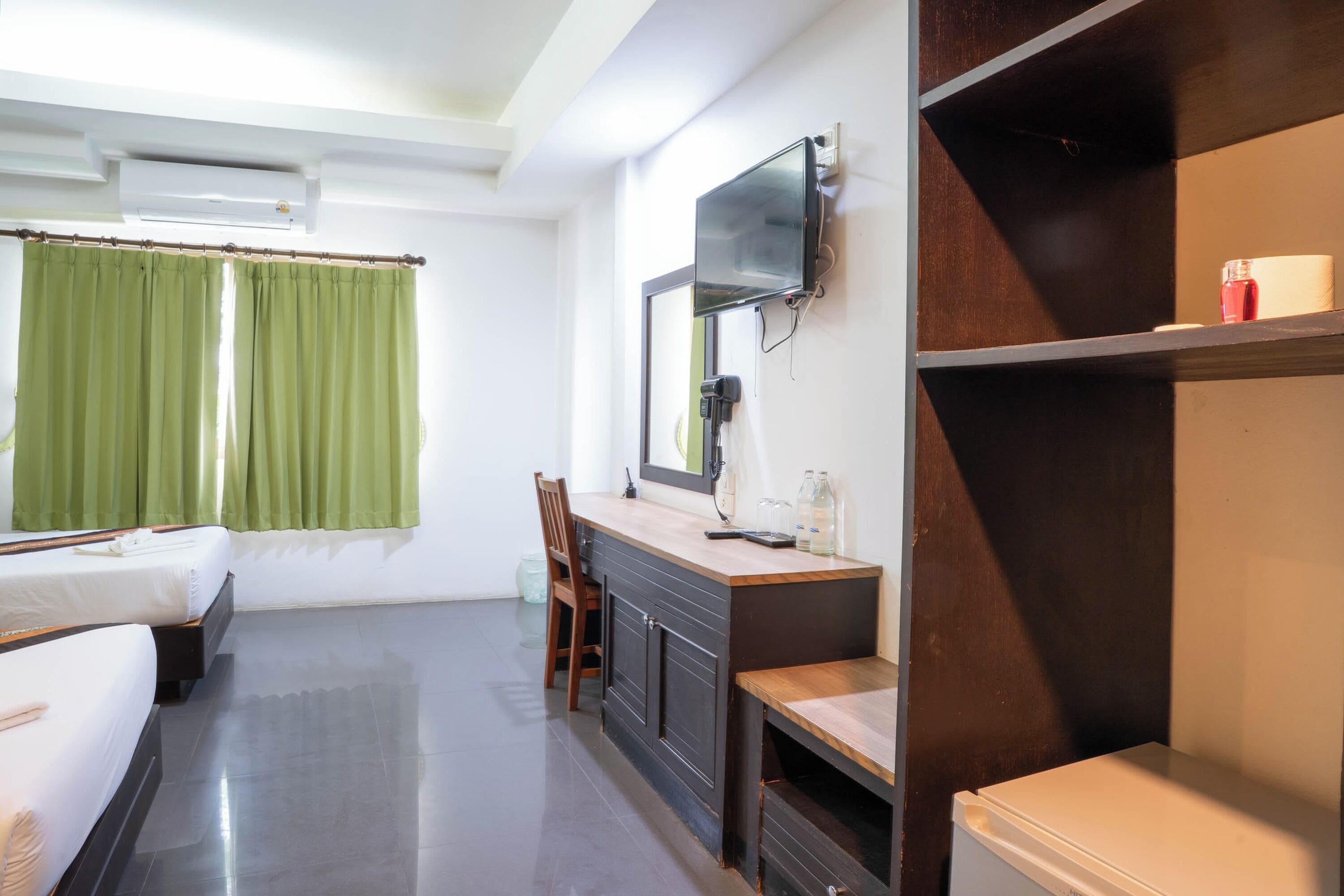 A hotel room with a bed, a desk with a mirror, a television, and a small refrigerator.