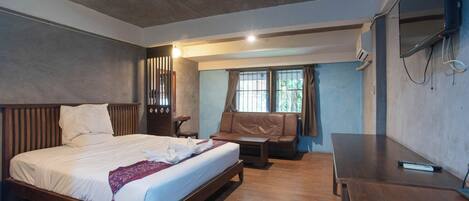 A modern bedroom with a wooden bed, a sofa, a desk, and a TV mounted on the wall.