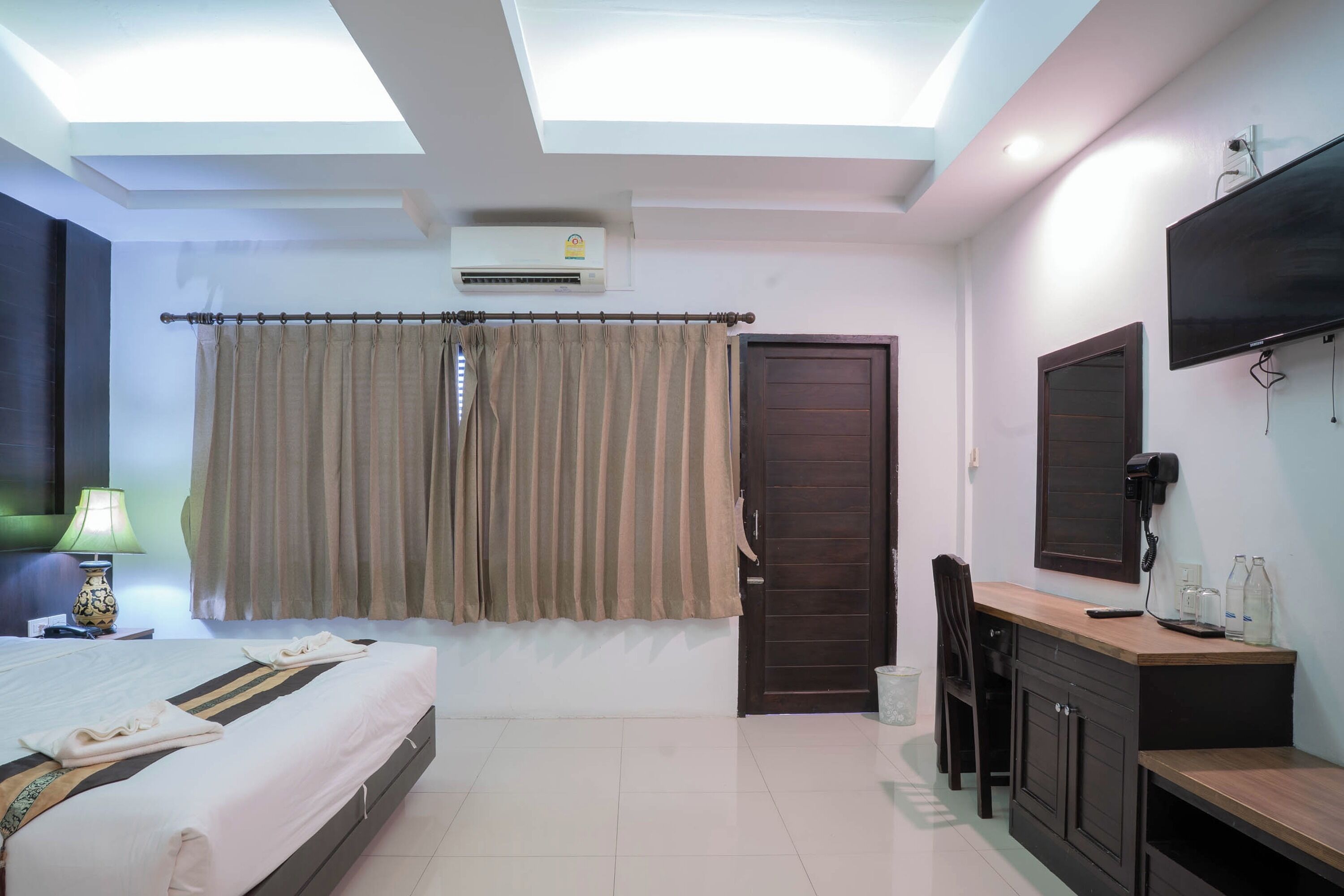 Habitación de hotel con cama, escritorio, silla, televisor y aire acondicionado.