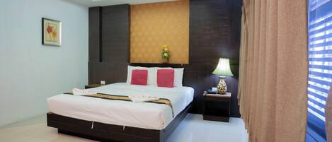 A modern hotel room with a large bed, a nightstand, a vase with flowers, and a window with curtains.