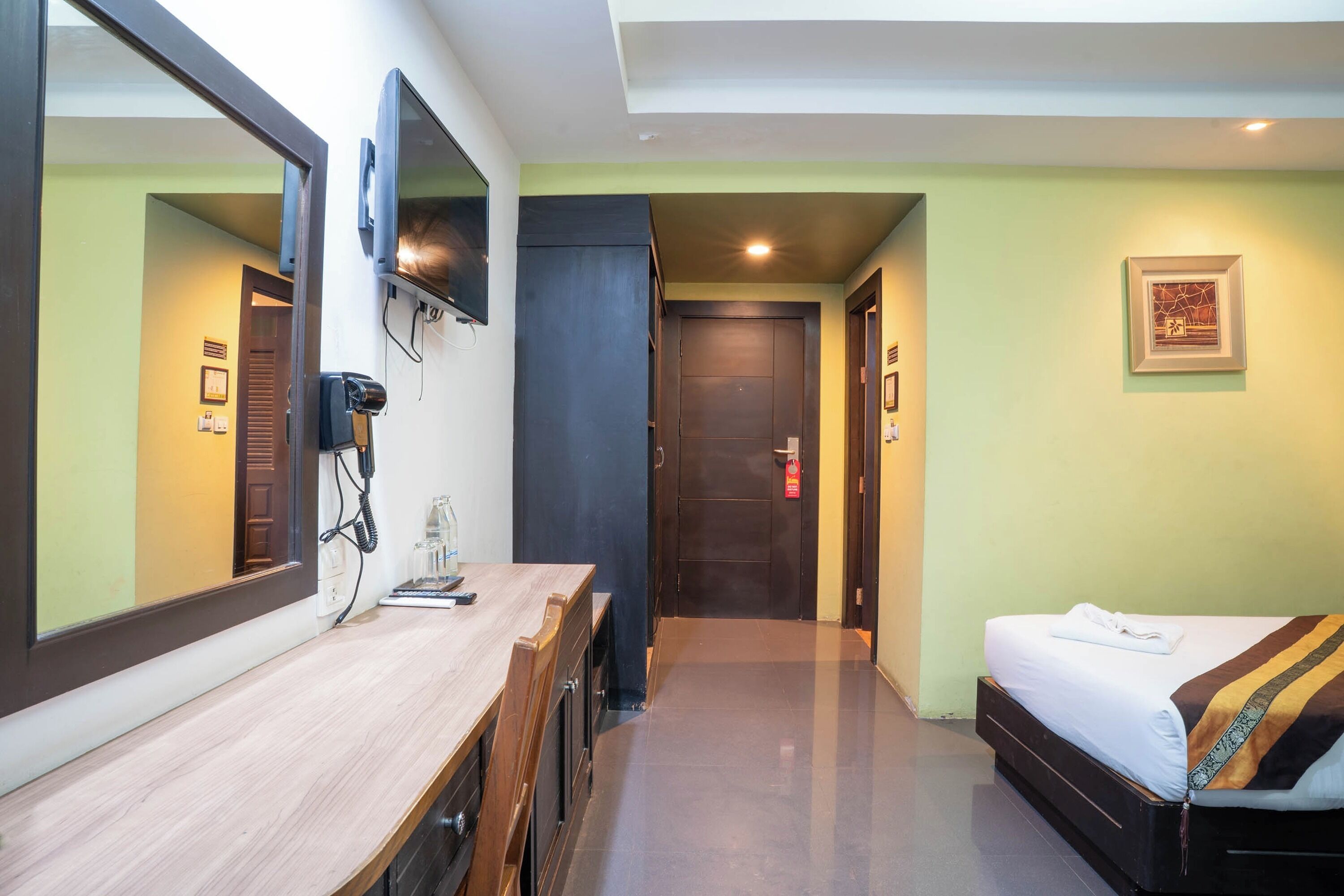 Une chambre d’hôtel avec un bureau en bois, un lit recouvert d’une couverture à rayures, un grand miroir et un téléviseur fixé au mur.