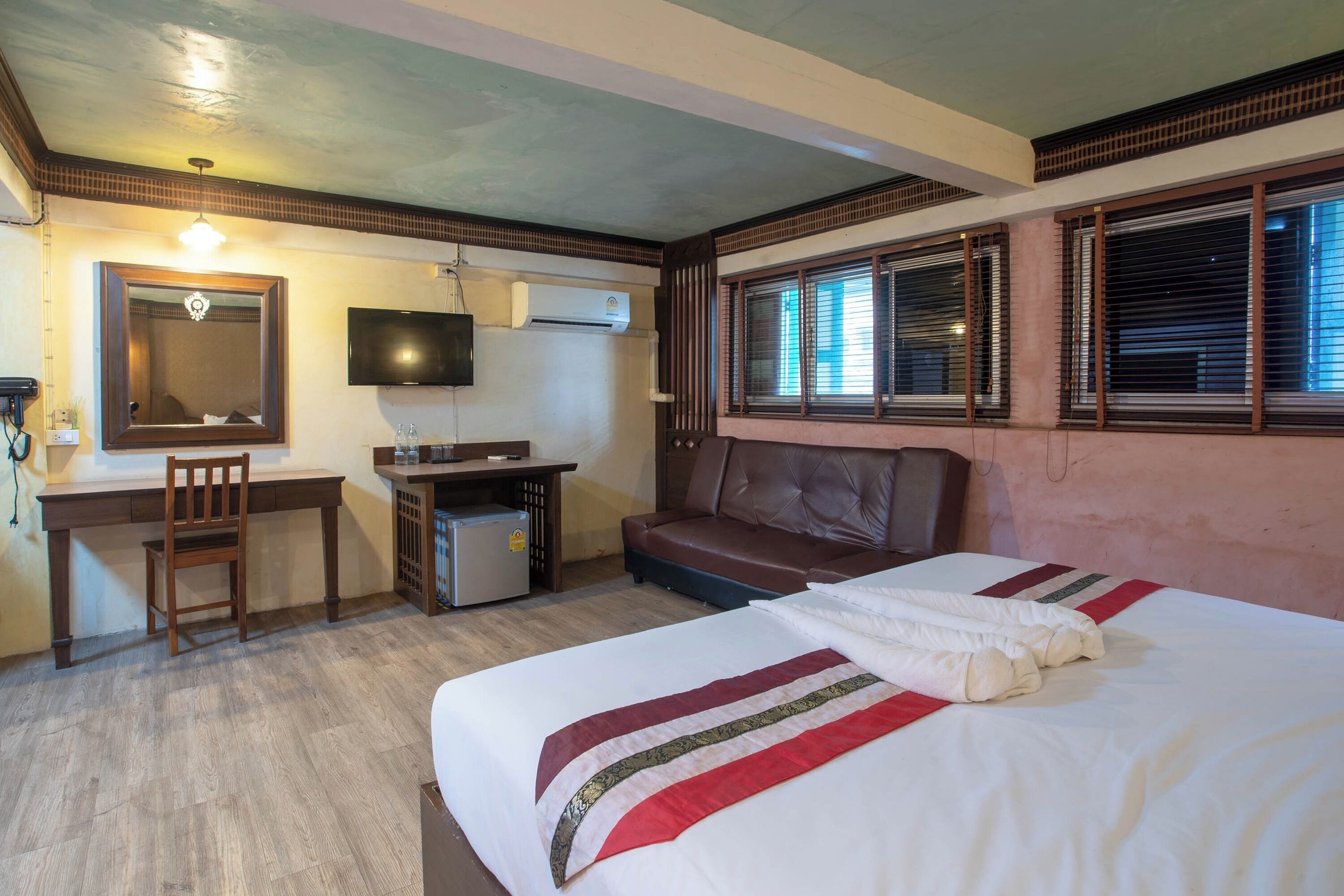 Une chambre d’hôtel équipée d’un lit, d’un bureau, d’une chaise, d’une télévision et d’une fenêtre avec des stores.
