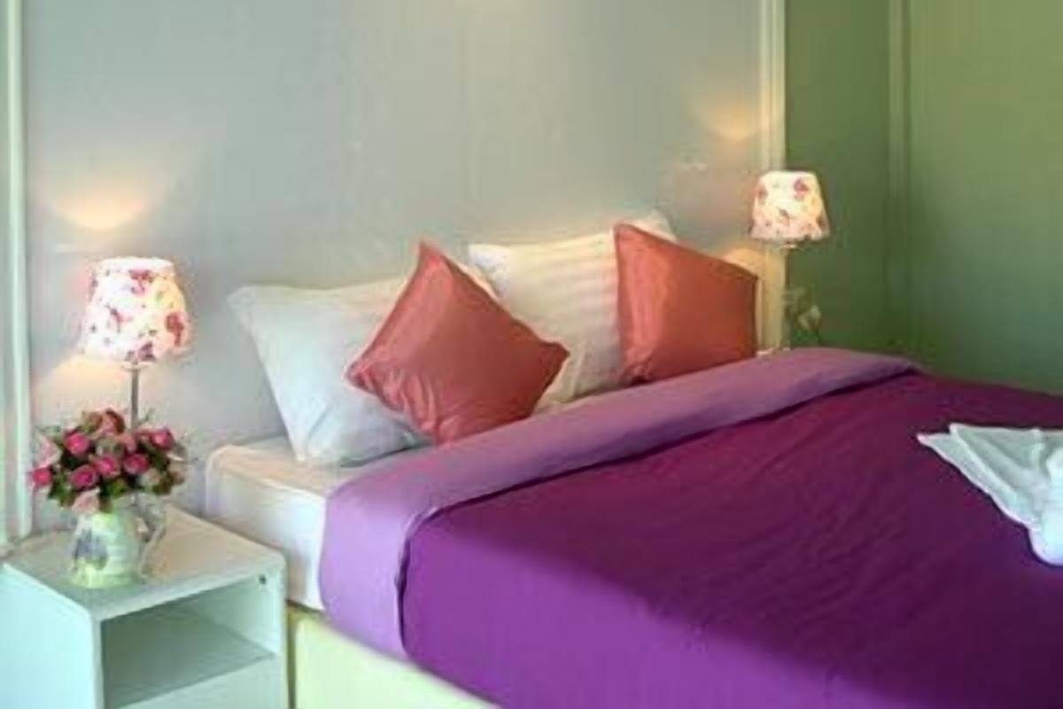 Una habitación de hotel con una cama, almohadas, una mesita de noche con una lámpara y un florero con flores.