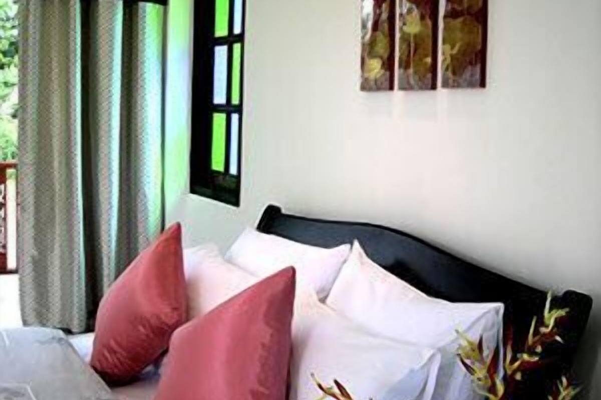 Una cama con cabecera negra, dos almohadas rojas y una blanca. Encima de la cama, hay tres obras de arte enmarcadas en la pared.
