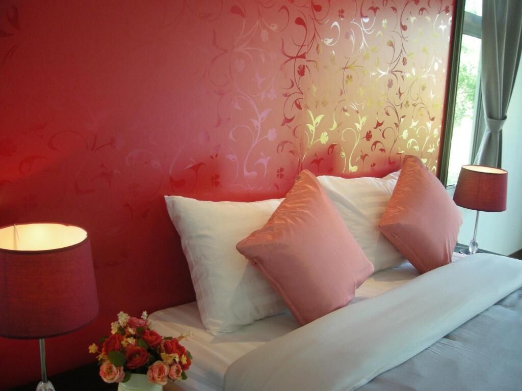 A bed with white and pink pillows, a vase of flowers, and two lamps on either side.