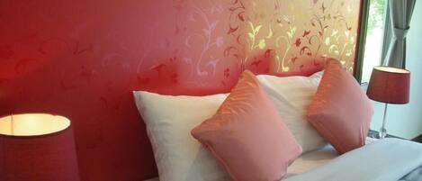 A bed with white and pink pillows, a vase of flowers, and two lamps on either side.