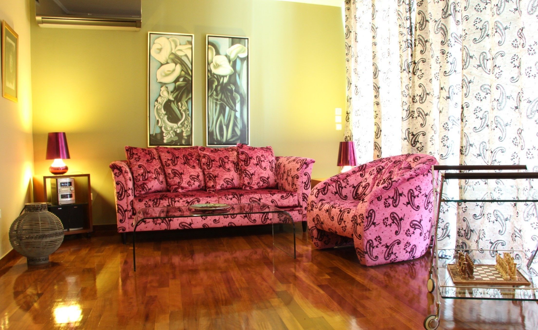 A living room with a pink patterned sofa, a glass coffee table, a chess set, a lamp, and a decorative vase.