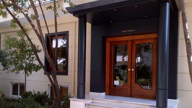 A building entrance with a wooden door, black columns, and a sign that reads "Apartments". - Andromeda Suites and Apartments (Athens)