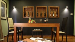 A dining area with a wooden table, two chairs, a fruit bowl, wine glasses, and a magazine on a rug. - Andromeda Suites and Apartments (Athens)