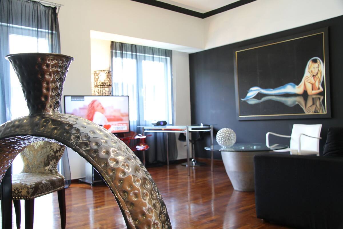 A modern living room with a large vase, a flat-screen TV, a painting, and a dining area.