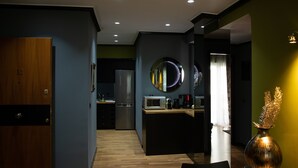 A modern kitchen with a refrigerator, microwave, and coffee maker. There is a wooden dining table and chairs. - Andromeda Suites and Apartments (Athens)