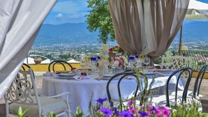 An outdoor dining setup with tables and chairs, overlooking a scenic view of a town and mountains. - Villa Casalguidi (Serravalle Pistoiese)
