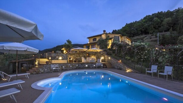 A swimming pool with lounge chairs and umbrellas, a stone staircase leading to a building, and a landscaped garden. - Villa Casalguidi (Serravalle Pistoiese)