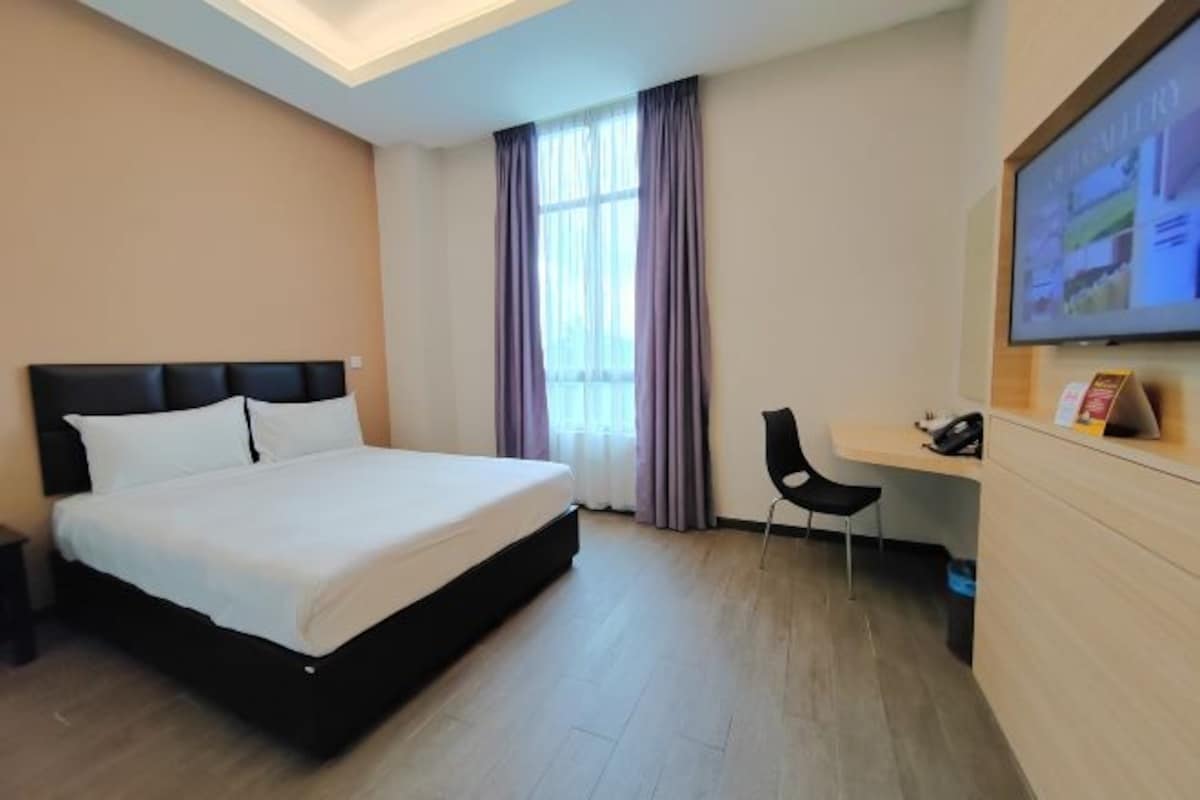 Habitación de hotel con cama, escritorio y televisión en la pared.