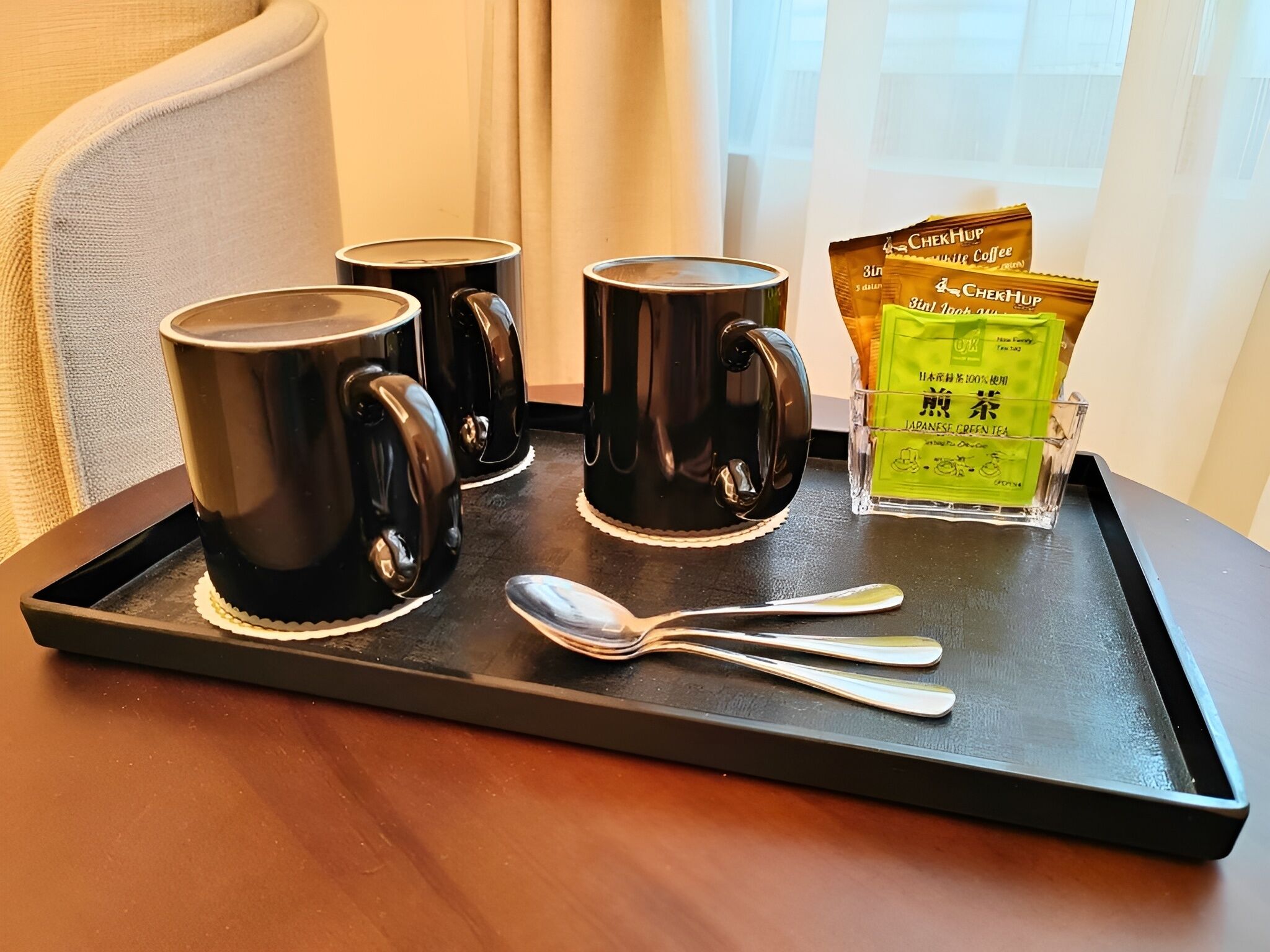 Una bandeja con tres tazas negras, un vaso de té verde japonés y una cuchara sobre una mesa de madera.