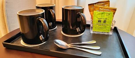Una bandeja con tres tazas negras, un vaso de té verde japonés y una cuchara sobre una mesa de madera.