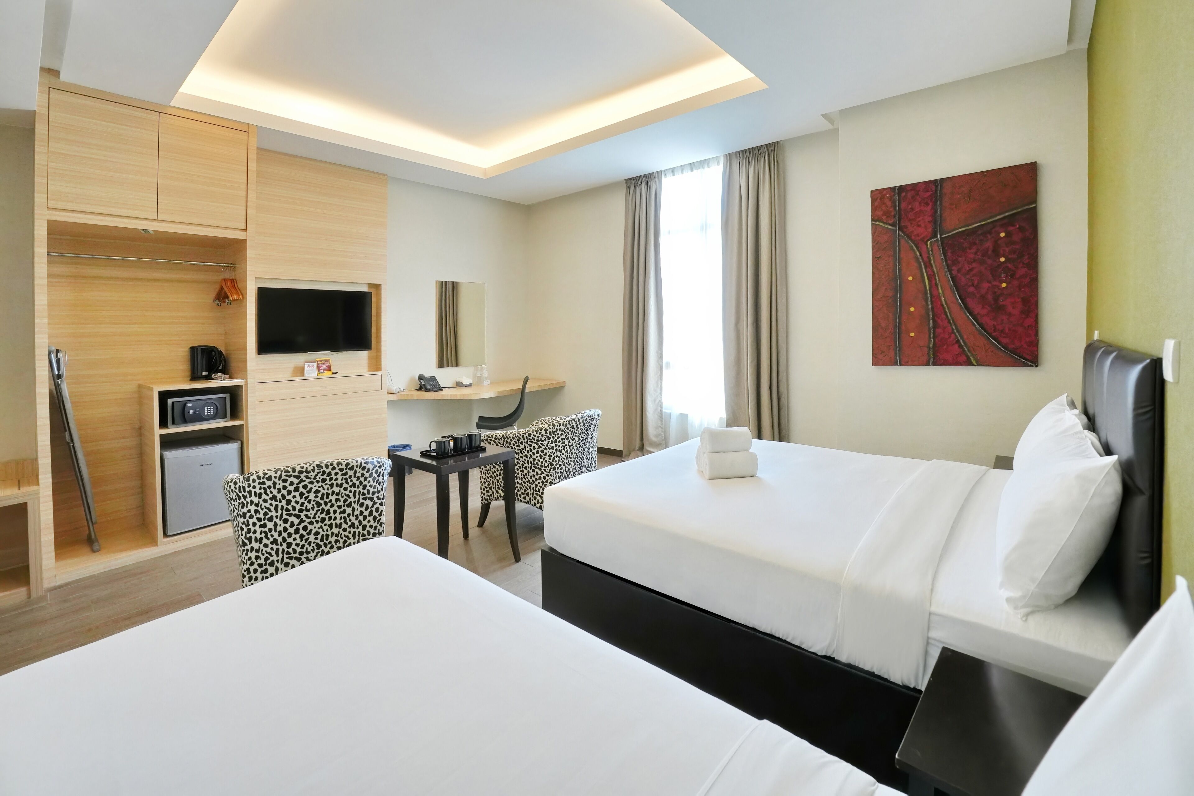 A hotel room with two beds, a desk, a chair, a TV, and a painting on the wall.