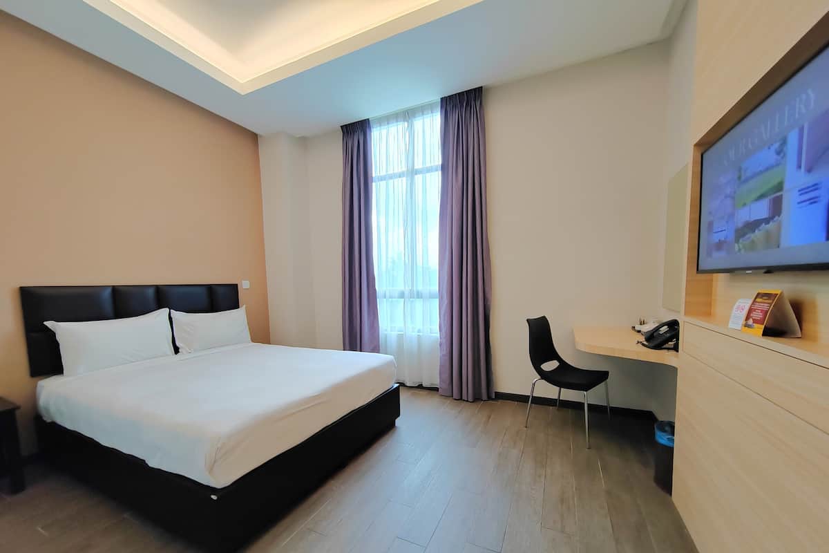 A hotel room with a bed, a desk, a chair, a television, and a window with curtains.