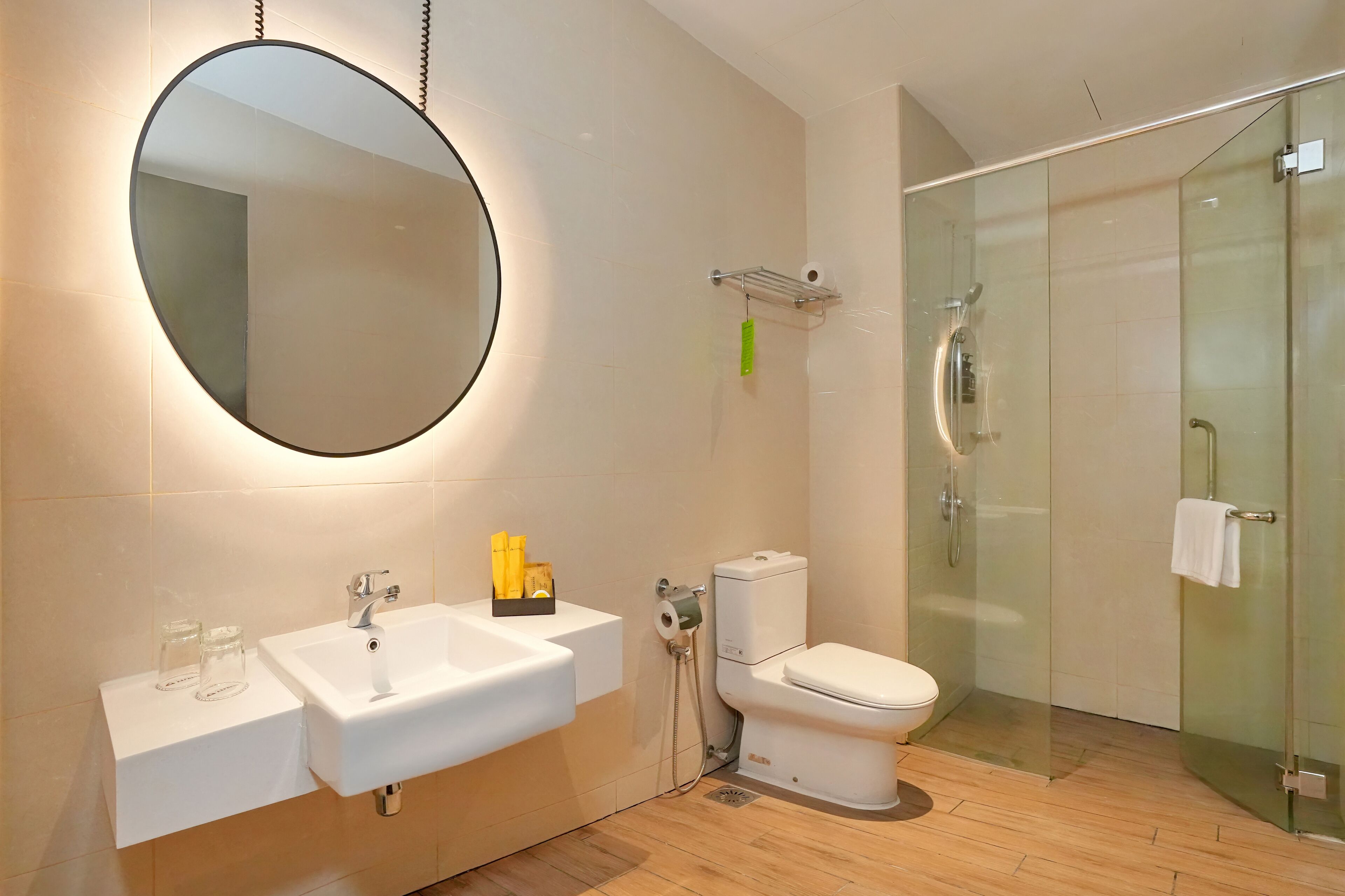 Un baño moderno con un espejo redondo, dos lavamanos, un inodoro y una ducha con cerramiento de vidrio.