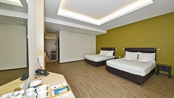 Een hotelkamer met twee bedden, een bureau met telefoon en waterfles, en een kleine kitchenette op de achtergrond.