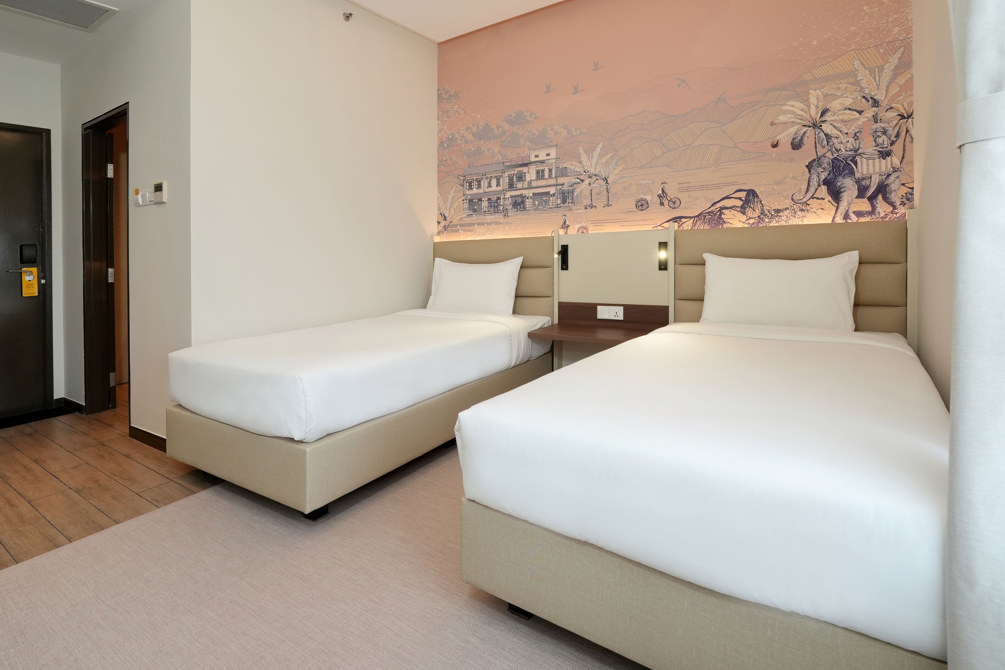 A hotel room with two beds, a wooden floor, a mural on the wall, and a door.
