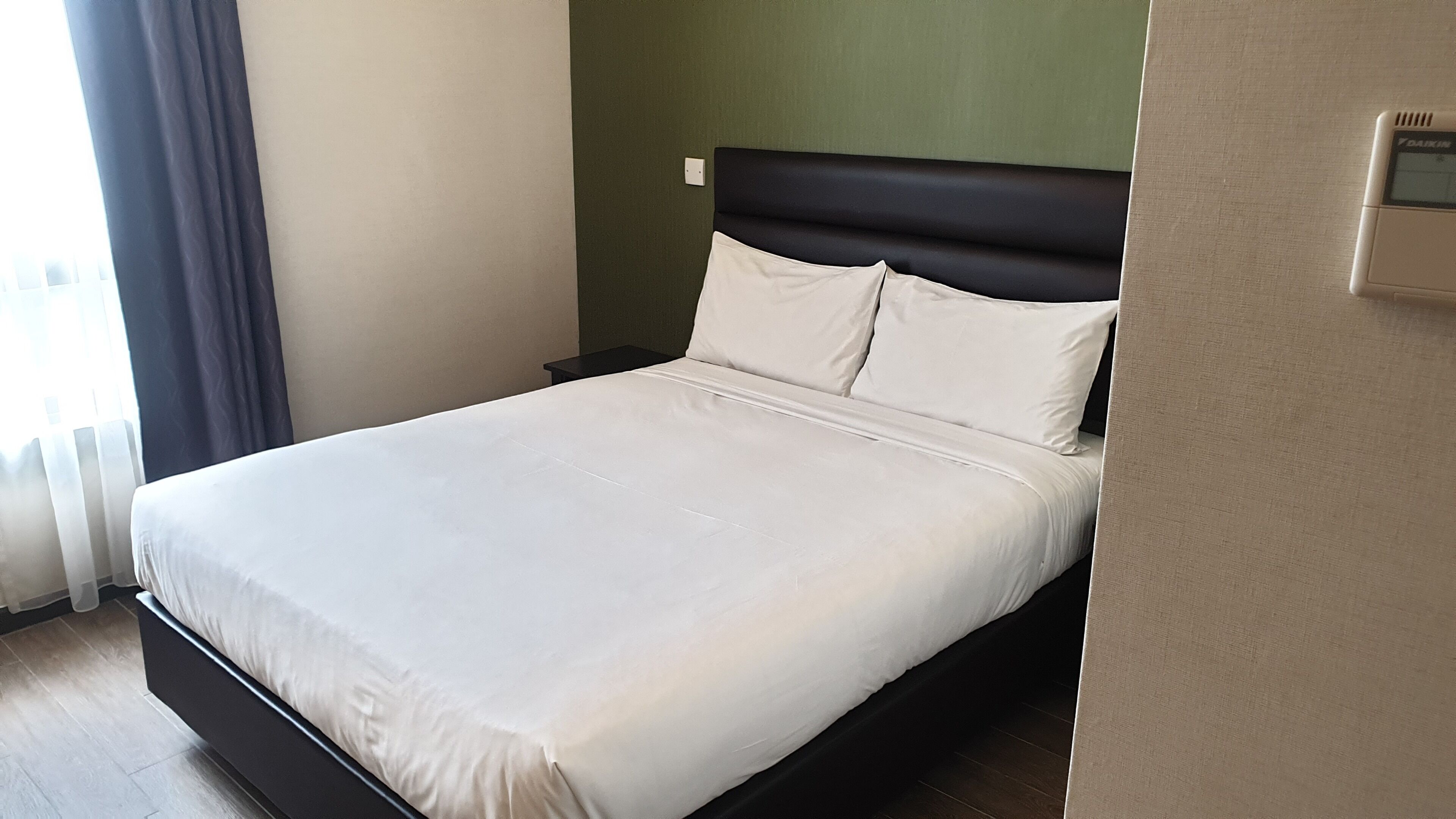 A modern hotel room with a single bed, a dark headboard, and a light-colored wall.