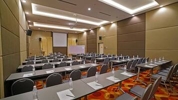 A conference room with rows of tables, chairs, and a projection screen.