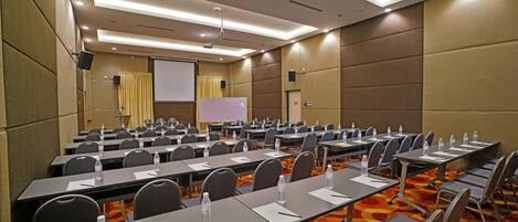 A conference room with rows of tables, chairs, and a projection screen.