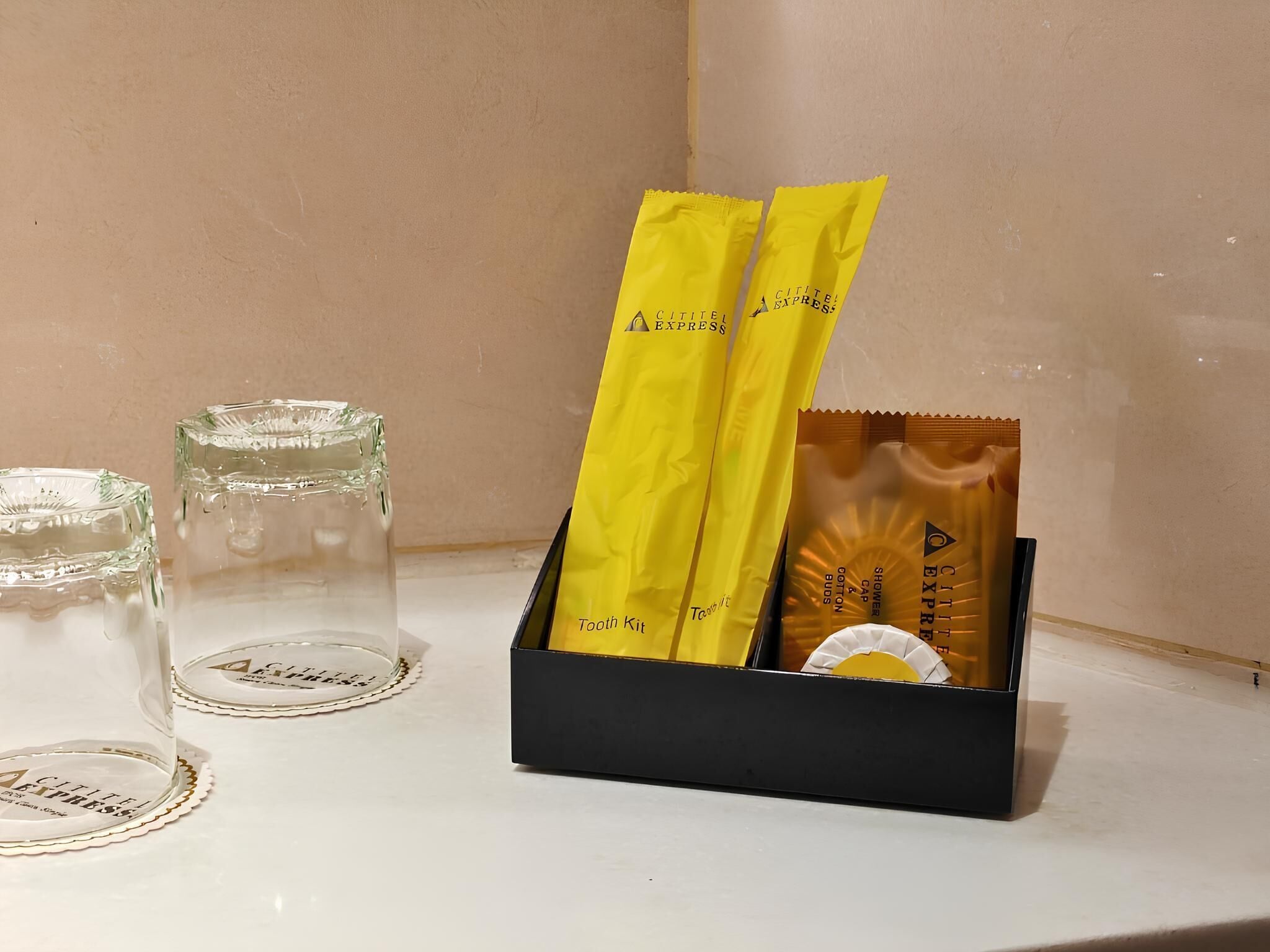 A black box containing a yellow toothbrush and a tube of toothpaste, with two empty glasses beside it.