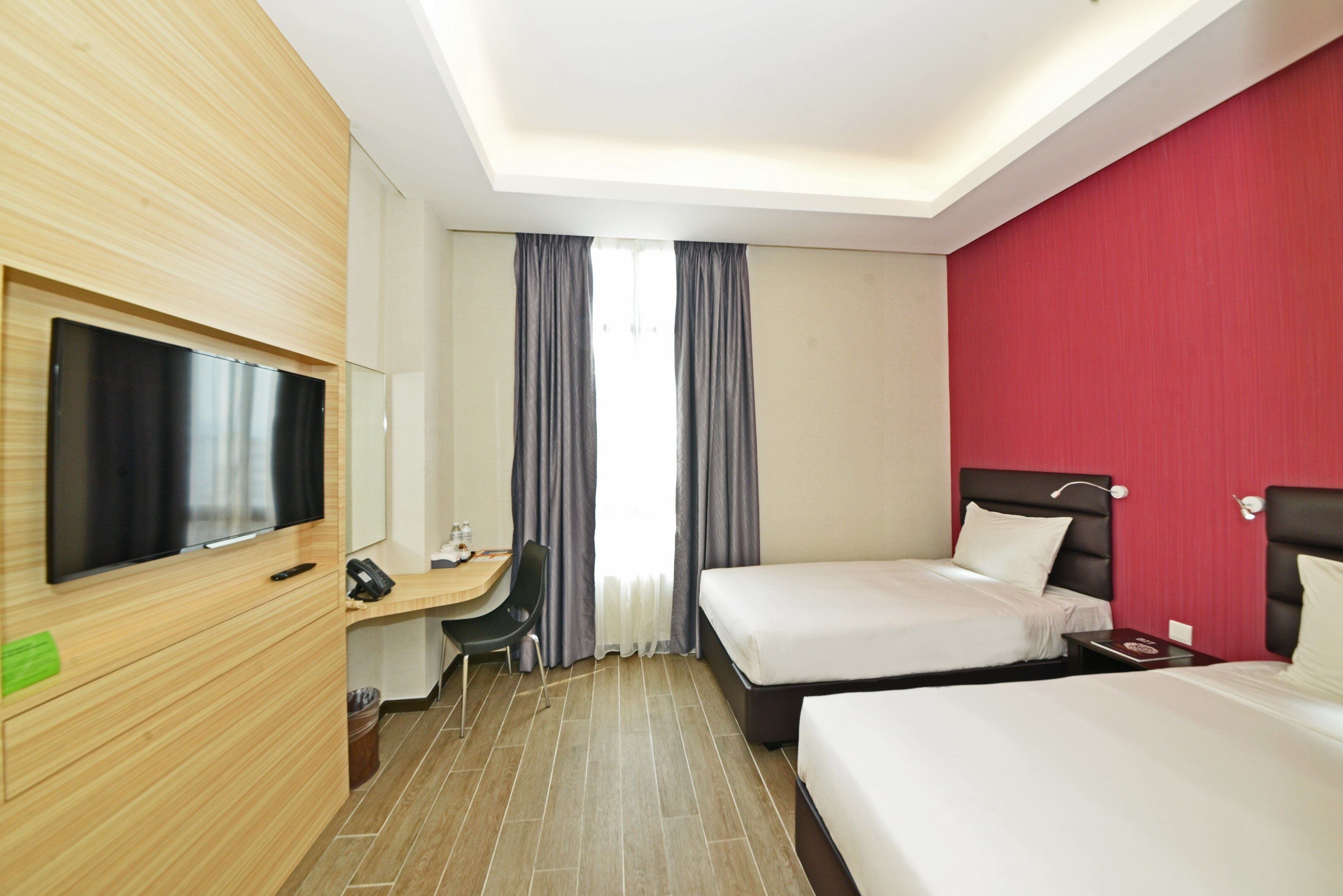 A hotel room with two beds, a desk with a chair, a television, and a red accent wall.