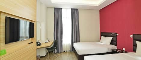 Quarto de hotel com duas camas, uma escrivaninha com cadeira, uma televisão e uma parede de destaque vermelha.