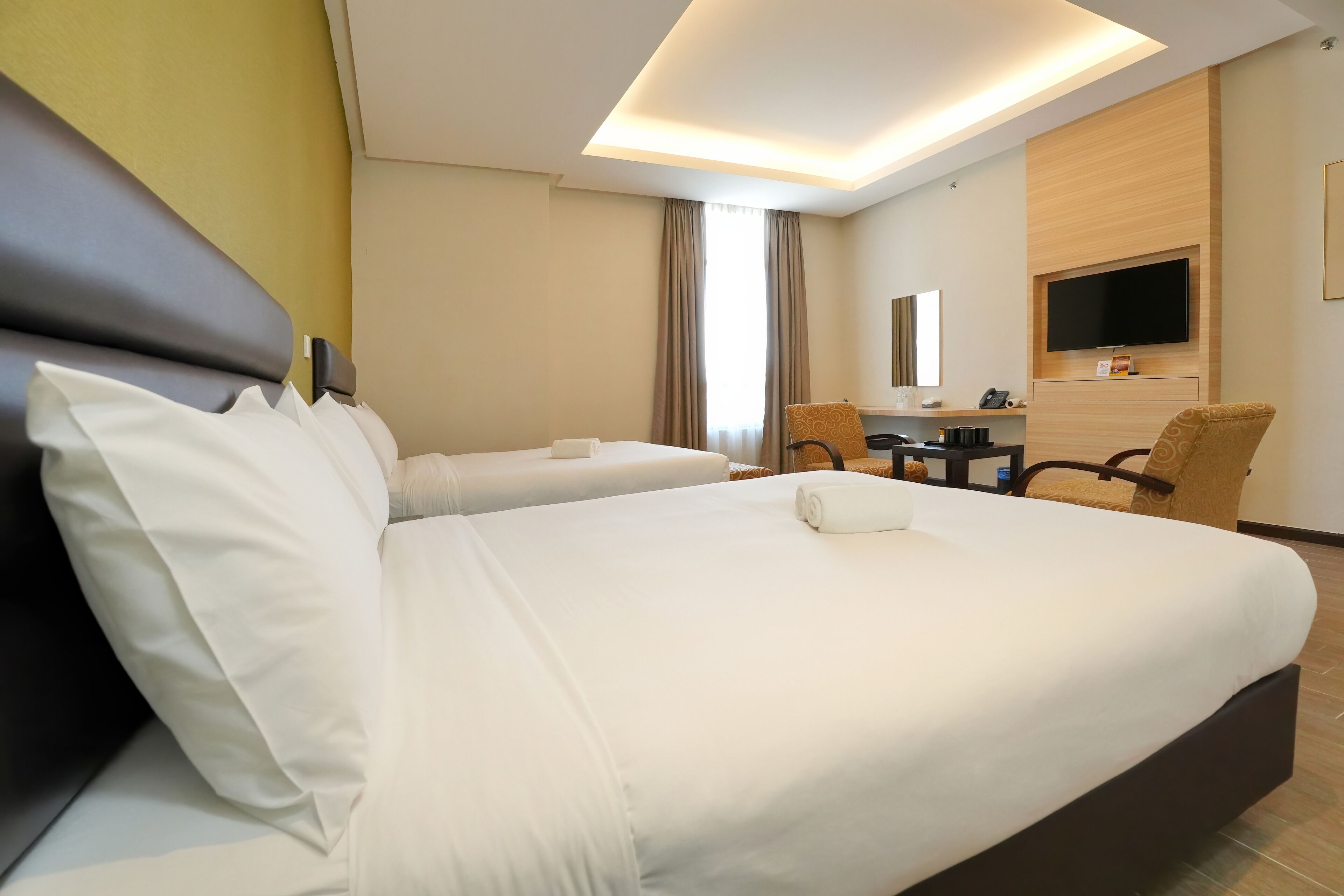 A hotel room with two beds, a desk, a chair, a TV, and a bathroom.